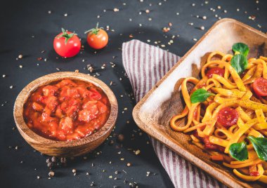 Tabakta domates soslu makarna. Koyu gri masada lezzetli bir porsiyon tagliatelle servis edildi.