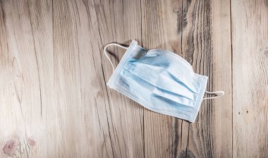 Tıbbi yüz maskesi. Ağzı ve burnu tahta arka planda kapatmak için plastik kulak bantlı tek kullanımlık cerrahi maske.