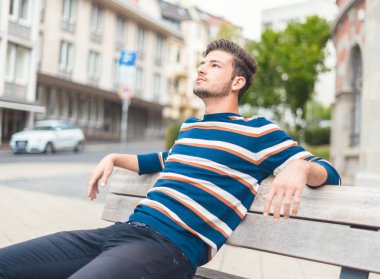 Bankta oturan genç ve güzel adamın yan görüntüsü. Yakışıklı adam, açık havada.