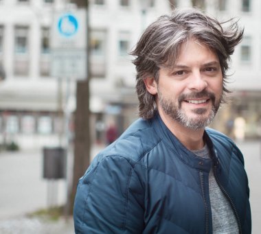 Kameraya bakan sakallı, yetişkin gülümseyen adam.