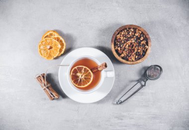 Fruit tea with cinnamon and dried orange in cup - teacup with strainer or percolator - filter isolated on gray background. Top view, overhead clipart