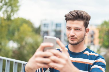 Yakından yakışıklı genç adam dışarıda akıllı telefonuyla fotoğraf çekiyor.