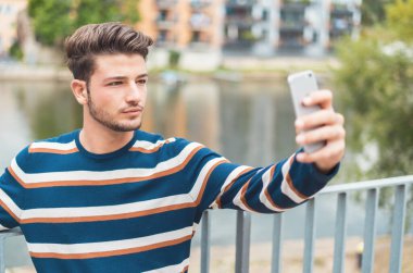 Yan görüş genç adam selfie çekiyor, açık havada.