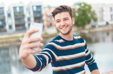 Sokaklarda kendi portresini çeken bir adam. Gülümseyen genç adam. Akıllı telefon özçekimi..