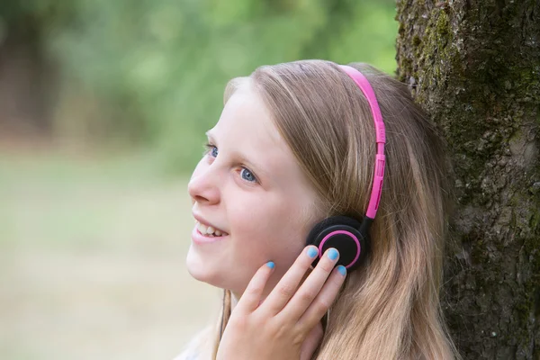 Chica sentada contra el árbol en el jardín escuchando música en Headph — Foto de Stock