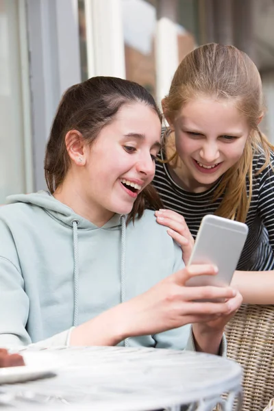 Two Young Girls At Cafe Reading Text Message On Mobile Phone — Stock Photo, Image