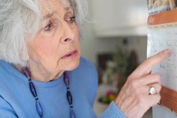 Verwirrte Seniorin mit Demenz blickt auf Wandkalender — Stockfoto