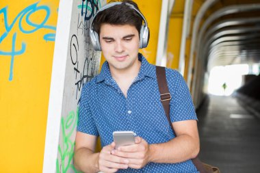 Cep telefonuyla kentsel ortamda kulaklıklar giyen genç adam