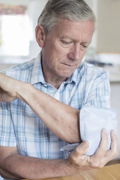 Oudere Man zetten ijskompres op de pijnlijke elleboog — Stockfoto