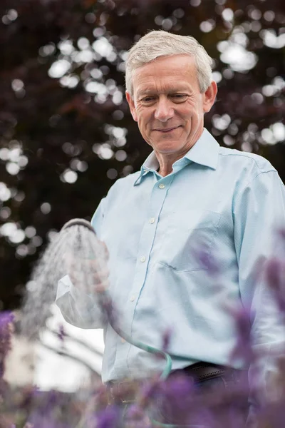 Senior Man Watering Flowers In Garden With Hose — Stock Photo, Image