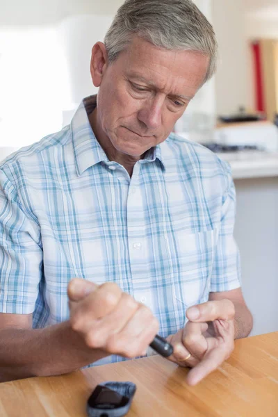 Зрелый человек проверяет уровень сахара в крови дома — стоковое фото