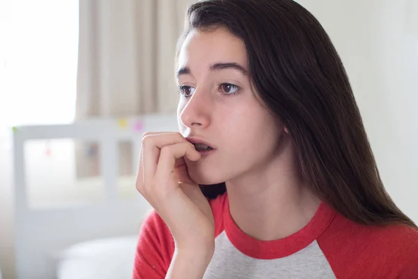 Menina adolescente sentada no quarto mordendo unhas — Fotografia de Stock