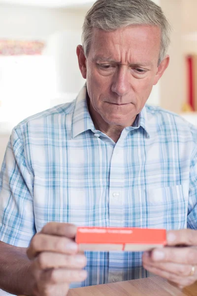 Homem maduro leitura informações sobre embalagem de drogas — Fotografia de Stock