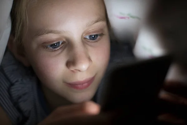 Fille à l'aide de téléphone portable se cachant sous la couette au lit la nuit — Photo