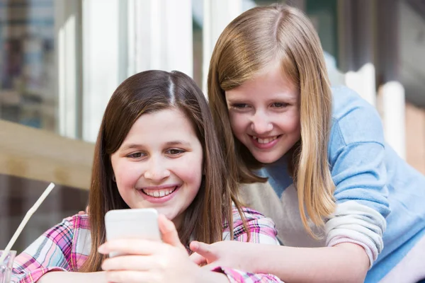 Two Young Girls At Cafe Reading Text Message On Mobile Phone — Stock Photo, Image