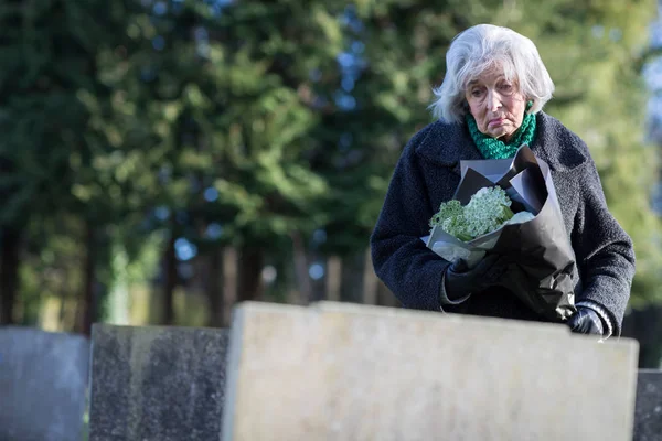 Сумно старший жінка з квітами, стоячи на могилі — стокове фото