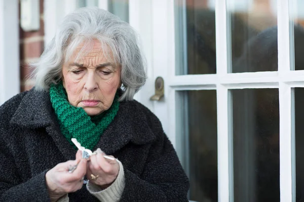 Запутавшаяся пожилая женщина пытается найти ключ от двери — стоковое фото
