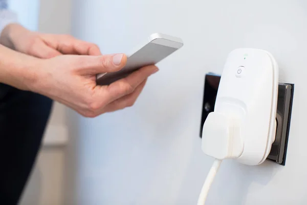 Женщина контролирует Smart Plug с помощью приложения на мобильном телефоне — стоковое фото