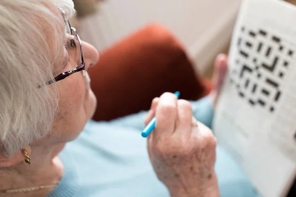 Seniorin beim Kreuzworträtsel zu Hause — Stockfoto