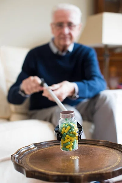 Starszy człowiek za pomocą osiągając ramię, aby podnieść leków w domu — Zdjęcie stockowe