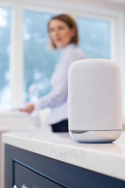 Woman In Kitchen Asking Digital Assistant Question Whilst Washin