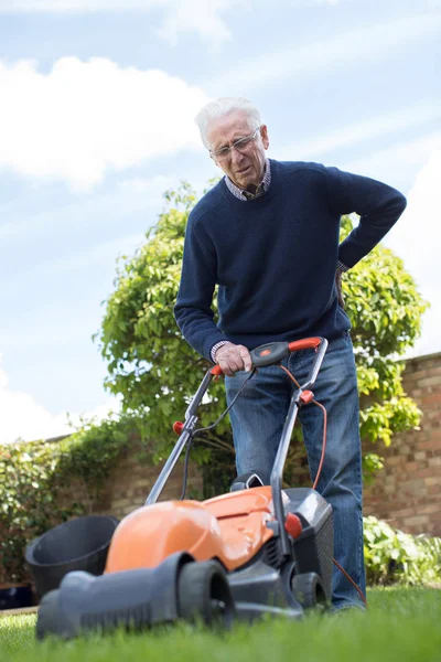 自宅の草をカットする電動の芝刈り機を使用しながら背中の痛みと苦しみを年配の男性 — ストック写真