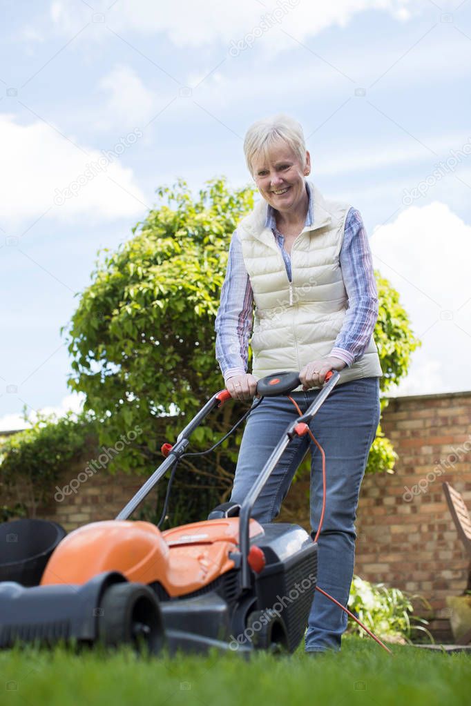 Senior Woman Using Electric Lawn Mower To Cut Grass At Home
