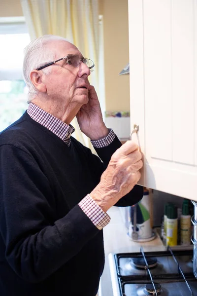 Forgetful Senior Man With Dementia Looking In Cupboard At Home — Stock Photo, Image