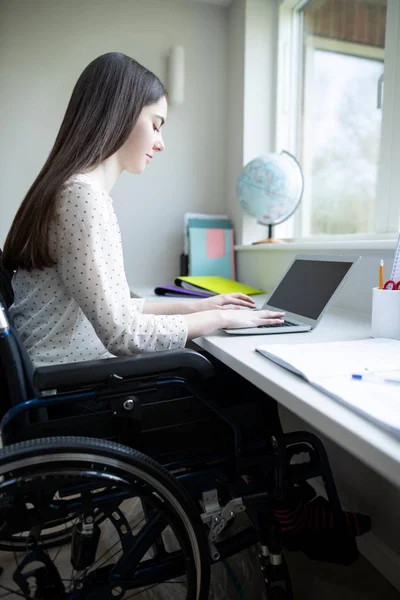 Teini tyttö pyörätuolissa opiskelu kotona kannettavalla tietokoneella — kuvapankkivalokuva