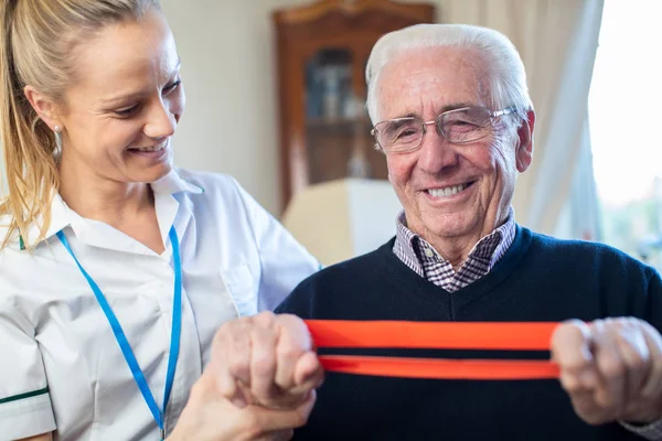 Γυναίκα Φυσικοθεραπεύτρια Βοηθώντας Senior Man To Use Resistance Band — Φωτογραφία Αρχείου