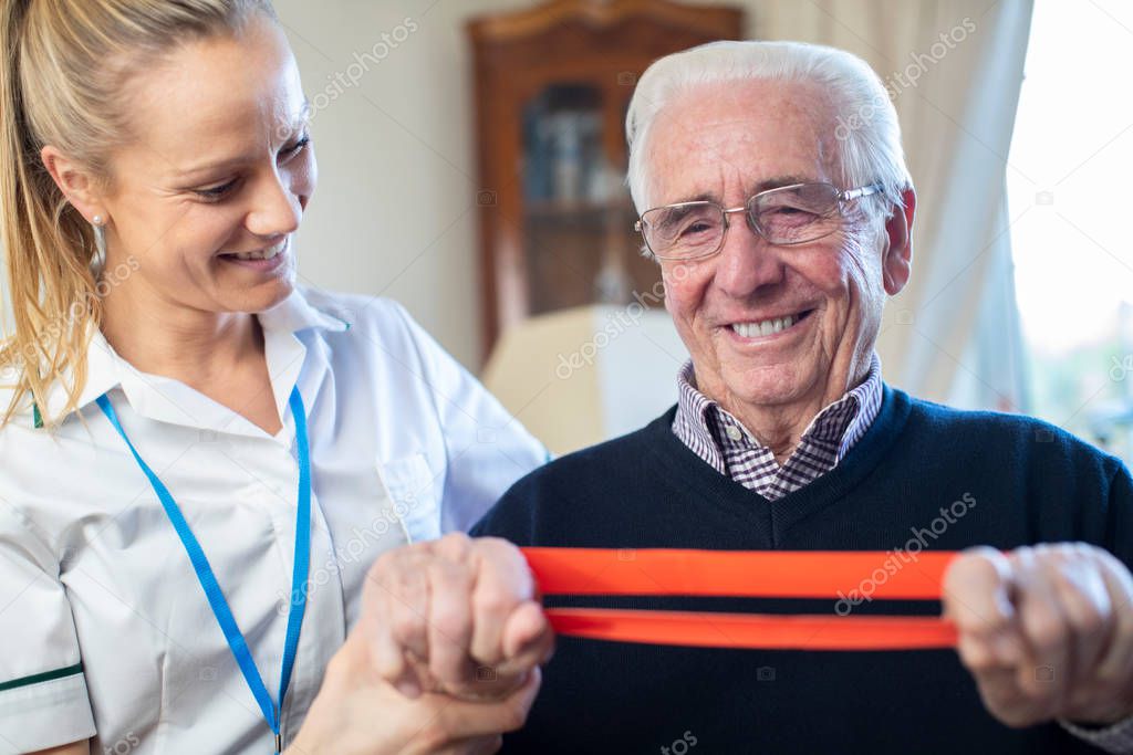 Female Physiotherapist Helping Senior Man To Use Resistance Band