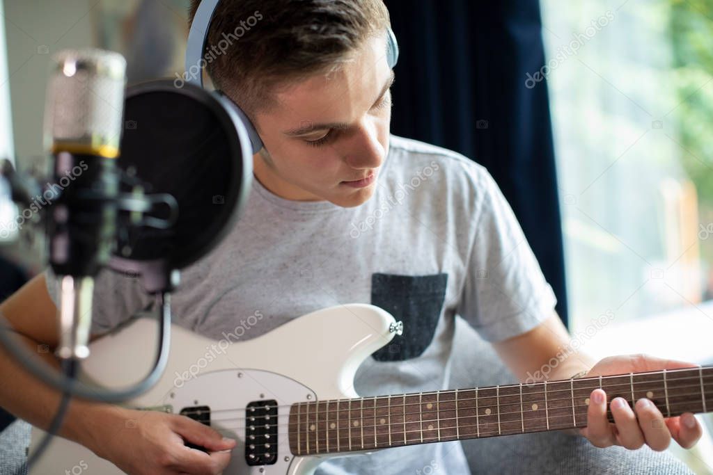Teenage Boy Playing Guitar And Recording Music At Home