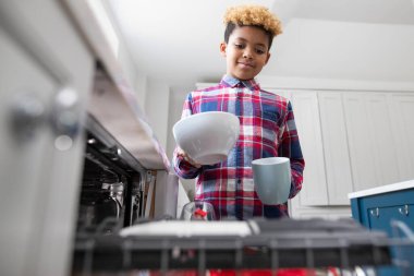 Bulaşık makinesine çanak çömlek istifleyerek Ev işlerinde yardımcı olan çocuk.