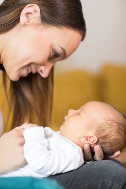 Sevgi dolu anne, bebek oğlunu koltukta kucaklıyor.