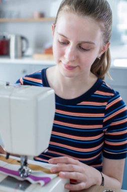Evde dikiş makinesini kullanmayı öğrenen genç bir kız.