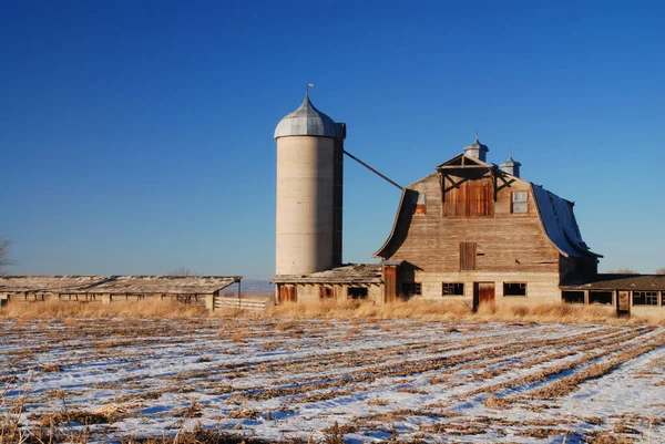 Alte verwitterte Scheune in der Nähe eines Silos unter dem klaren blauen Himmel und behi — Stockfoto