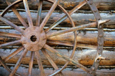 Large Metal Spiked Wagon Wheel leaning against a log wall