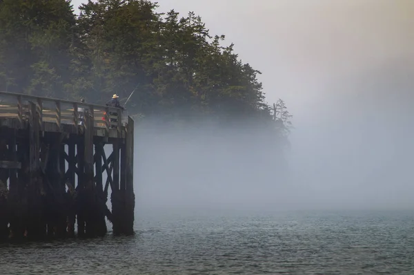 Man in Hat Fishing off the peer and into the mist covered water — Stok Foto
