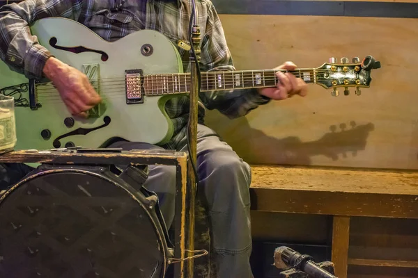 Man playing a greenish guitar while sitting on a wooden bench — Stock Photo, Image