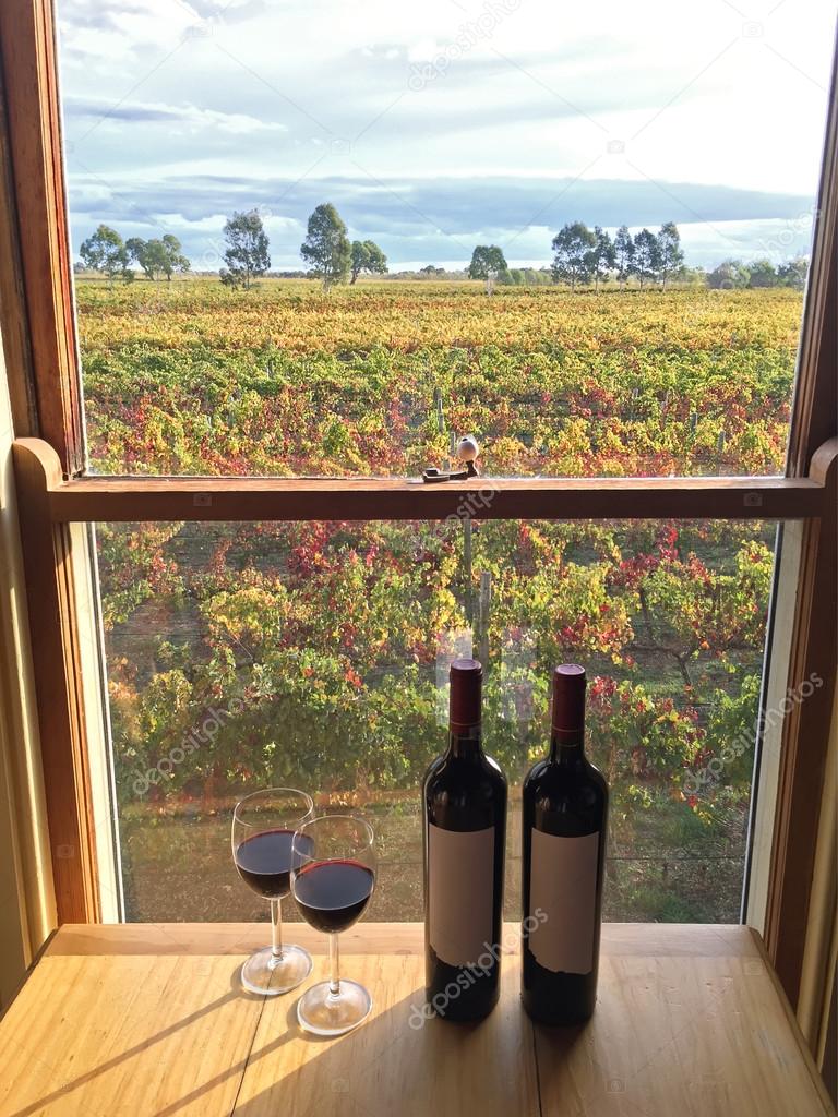 Glass of red wine next to bottles near windows with soft view of vineyard, South Australia