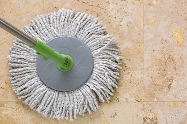 Used round spin mop with microfiber head, green handle on yellow granite tiles floor clipart