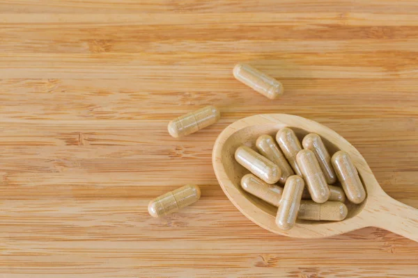 Colher de madeira cheia de ervas medicinais em cápsulas claras, ideal para remédios homeopáticos — Fotografia de Stock