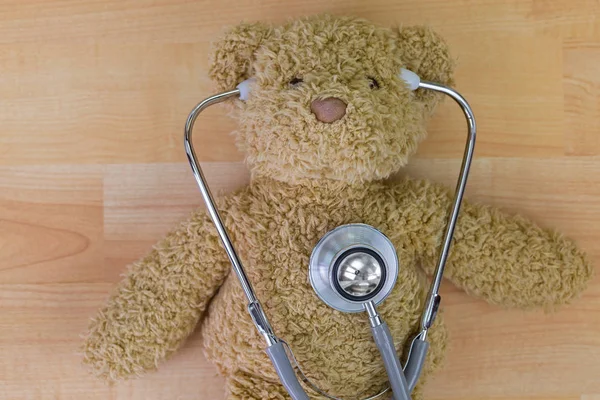 Teddy bear on wooden floor with stethoscope with earpieces in ears