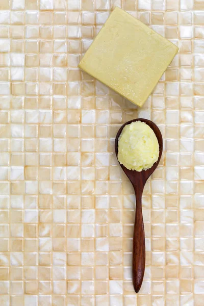 Shea butter in wooden spoon,  homemade olive oil soap on yellow tile background