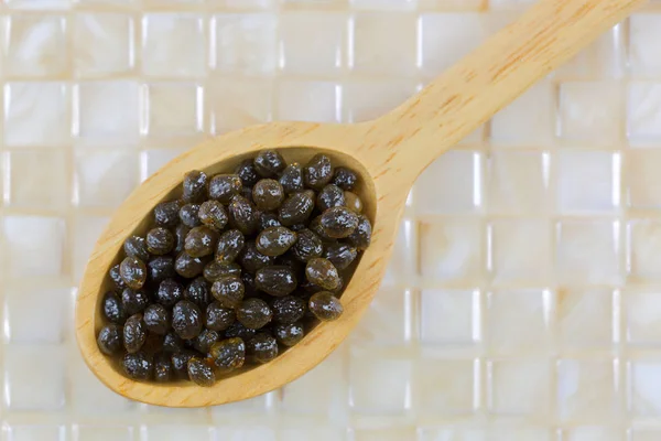 Closeup of fresh papaya seeds in wooden spoon on yellow tile — Stock Photo, Image