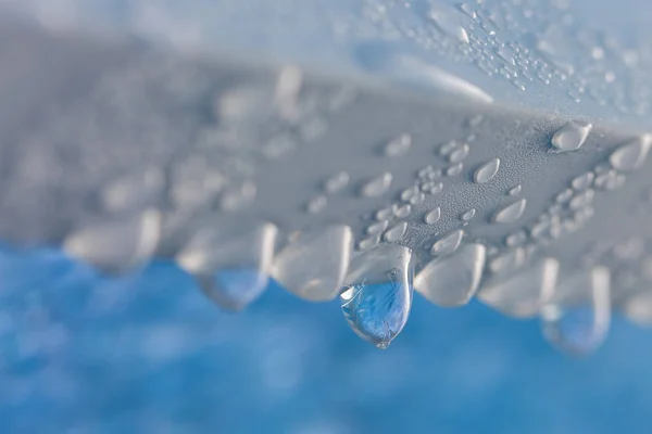 Drop of frozen water dripping from the blue ceiling