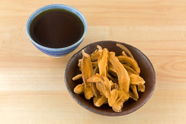 Tigela de ervas cortadas em fatias seco cogumelo Lingzhi ao lado do chá quente Reishi — Fotografia de Stock