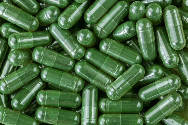 Green Spirulina powder, blue-green algae in clear capsules — Stock Photo, Image