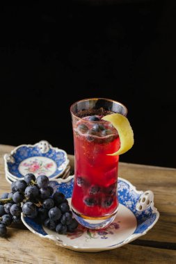 Cranberry color cocktail  garnished with fresh grapes on a vinta