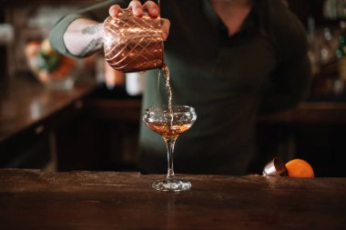 A bartender pouring a cocktail in a glass 